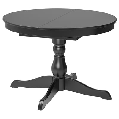 Une table à manger ronde et extensible noire INGATORP avec un design de pieds tournés. Il est fait de matériaux comme le bouleau massif et les panneaux de particules.