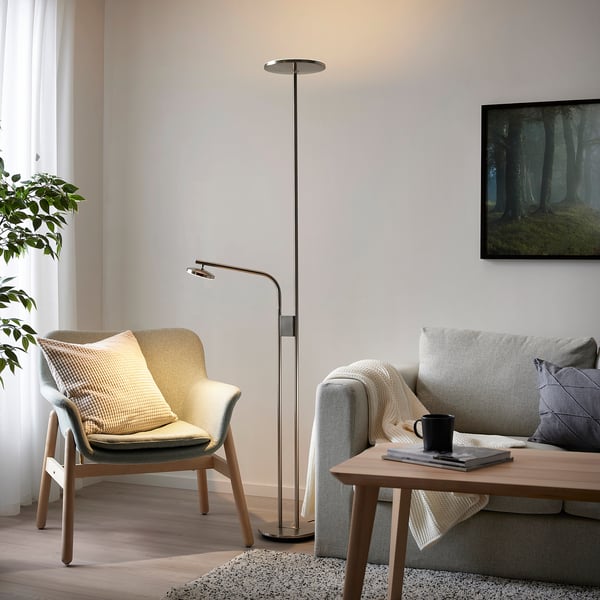 Salon moderne avec lampe, canapé, fauteuil, plante et imprimé forêt. Confortable, minimaliste.