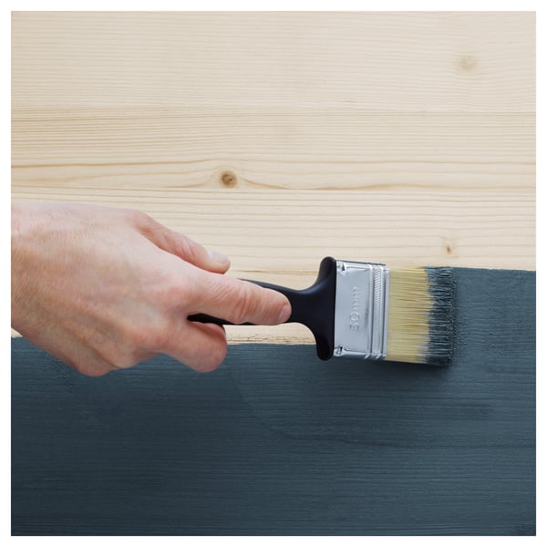 La personne peint une planche de bois avec un pinceau. Le bois semble être de la marque IVAR, connue pour ses propriétés durables, ponçables et naturelles.