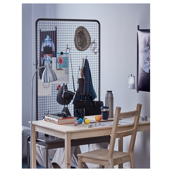 Bureau en bois avec chaise, avec divers objets comme une lampe, un appareil photo et des livres. Un panneau de grille est suspendu derrière, affichant des notes et des sacs.