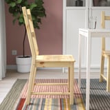 Chaise en bois près de la table blanche sur tapis rayé. Chambre lumineuse et minimaliste avec plante.