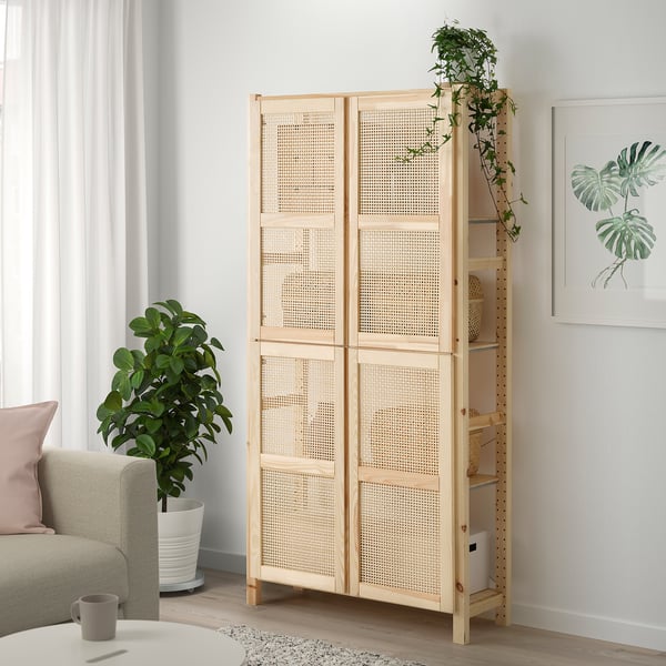 Étagère IVAR avec portes en bambou, pin, debout à côté des plantes et du canapé gris.