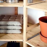 Étagère en bois avec coussins et casseroles, mettant en valeur le rangement polyvalent d’IVAR.