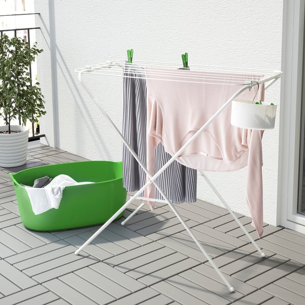 Un étendoir pliable blanc avec des vêtements, doté d’un panier vert avec du linge, adapté à une utilisation intérieure ou extérieure.