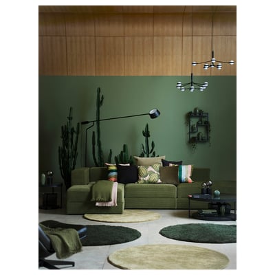 Ensemble de canapé moderne dans un salon élégant avec des murs verts, des décalcomanies de cactus et des tapis vibrants. Sièges profonds, plaids, table basse et table d’appoint.
