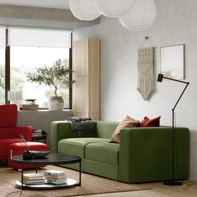 Salon moderne avec canapé JÄTTEBO vert olive, chaises rouges, armoires en bois et lampadaire.
