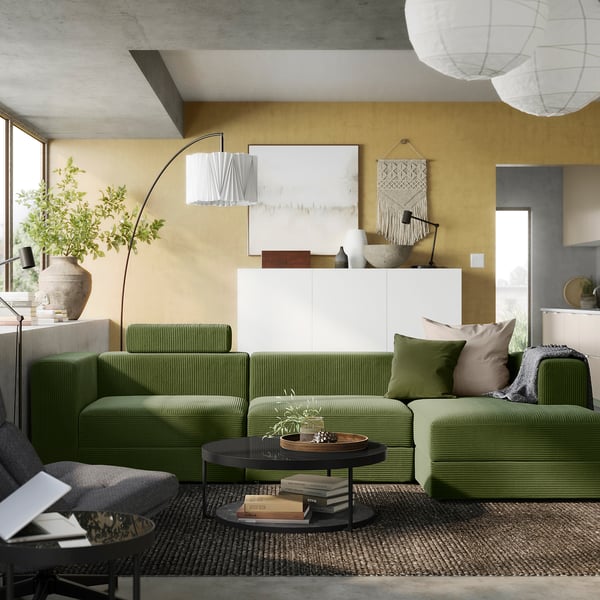 Salon moderne avec canapé olive, plante, lampes, art, tapis, béton.