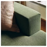 Détail du canapé en velours côtelé vert, coussins moelleux, parquet.