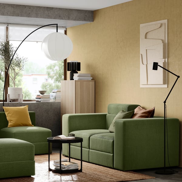 Salon moderne : canapé en velours côtelé vert, oreiller jaune, armoire en bois, art abstrait, grand lampadaire.