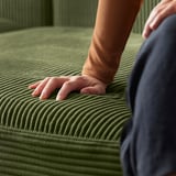 La personne touche un canapé en velours côtelé vert avec siège de rangement.