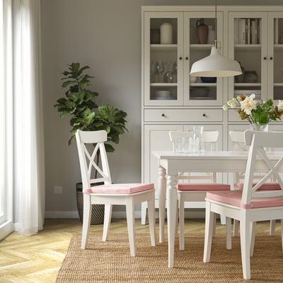 Salle à manger avec chaise JUSTINA, coussins roses, plante et fleurs. Élégant et confortable.