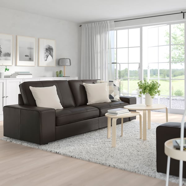 Salon moderne avec un canapé KIVIK spacieux gris foncé, des coussins clairs, des tables en bois et de grandes fenêtres.