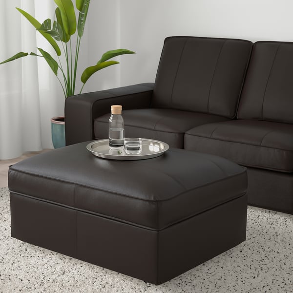 Salon moderne avec canapé en cuir noir KIVIK et pouf ; Ottoman a un plateau avec une bouteille et un verre, plante à proximité.