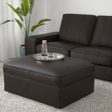 Salon moderne avec canapé en cuir noir KIVIK et pouf ; Ottoman a un plateau avec une bouteille et un verre, plante à proximité.