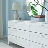 Commode blanche avec 6 tiroirs et lampe, contre les murs bleus.
