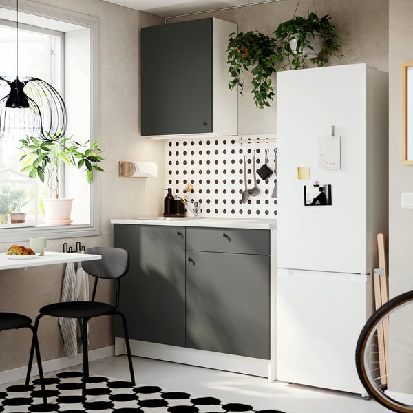 Cuisine moderne : armoires grises, comptoir en marbre, accents noirs, plantes suspendues, sous la fenêtre, grand réfrigérateur.