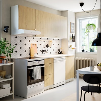 Cuisine moderne avec bois, appareils électroménagers blancs, accents noirs. Four en acier inoxydable, suspension, plante. Dosseret à pois noirs, comptoir blanc.