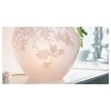 Une lampe de table ronde et blanche nommée KNUBBIG avec un motif de fleurs de cerisier gravé, créant une douce lumière d’ambiance.