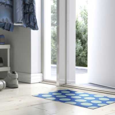 Tapis KÖRFÄLTSPIL bleu avec cercles blancs, de grande taille, près de la porte.