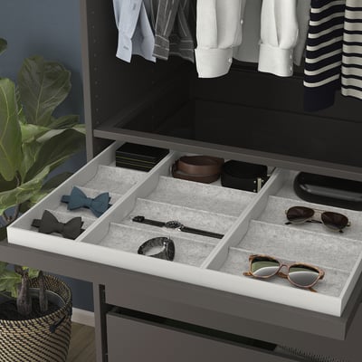 Tiroir ouvert montrant le plateau KOMPLEMENT avec des compartiments doublés de feutre pour ranger des montres et des lunettes de soleil.