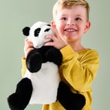 Un jeune garçon, vêtu d’une chemise jaune, sourit en tenant un panda en peluche noir et blanc.