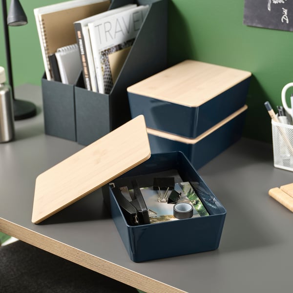 Trois boîtes bleues KUGGIS faites de plastique recyclé et de bambou, rangeant et empilant soigneusement les fournitures de bureau.