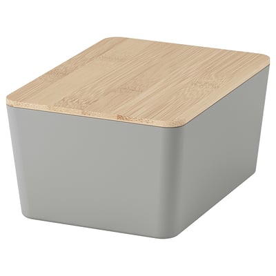 Une boîte de rangement KUGGIS gris clair avec un couvercle en bambou naturel, de forme rectangulaire, conçue pour organiser les petits objets.
