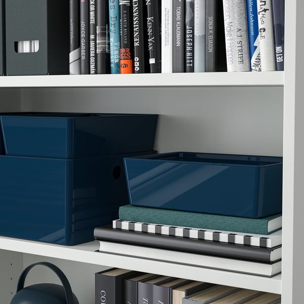 Bibliothèque avec des cartons en plastique bleu et une pile de livres, montrant un rangement organisé et une protection contre la poussière.