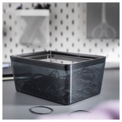 Boîte en plastique gris KUGGIS sur un évier, de forme rectangulaire, couvercle transparent, contenant des accessoires pour cheveux.