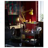 Bureau à domicile moderne avec chariot de cuisine en acier inoxydable KUNGSFORS, lampe jaune, ordinateur, snacks et rideaux rouges.