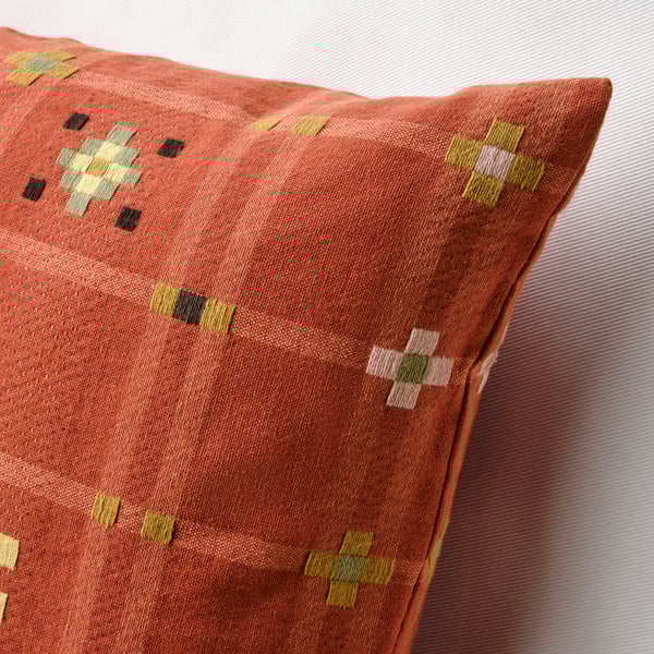 Gros plan de la housse de coussin KUSTGRAN en rouge, présentant un motif de ceinture de moine tissé complexe, une texture en coton de qualité et des détails de fermeture éclair cachés.