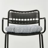 Chaise en osier noir avec coussin à motifs, siège d’extérieur élégant et durable.