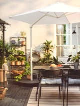 Patio extérieur avec chaises LÄCKÖ noires, parasol blanc et diverses plantes en pot.