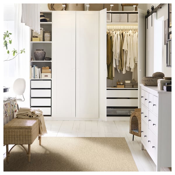 Chambre avec armoire intégrée, tiroirs blancs, banc en osier et tapis beige.