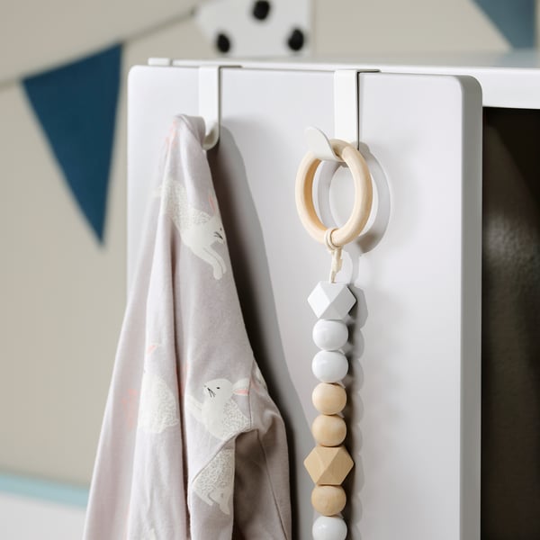 Un crochet LÄTTHET blanc avec une couverture suspendue et un jouet en perles de bois.