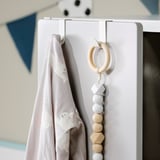 Un crochet LÄTTHET blanc avec une couverture suspendue et un jouet en perles de bois.