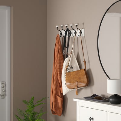 Support LANDKRABBA noir avec 5 crochets, contenant un pull orange, un sac et des bretelles. À côté de la commode et du miroir.