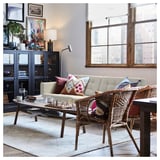 Salon moderne avec un canapé LANDSKRONA beige, une chaise tressée, une table basse en bois et de grandes fenêtres. Des coussins décoratifs et un jeu d’échecs sur la table.