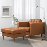 Fauteuil en cuir marron, pouf, grande lampe, mur blanc, art, fleurs.