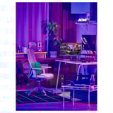 Une configuration de bureau de jeu colorée avec une chaise ergonomique LÅNESPELARE en vert, des écrans d’ordinateur, des néons et des plantes.