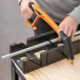 Personne utilisant un outil à manche orange pour couper un panneau de bois avec un appareil de mesure noir.