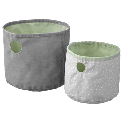 Deux bacs de rangement en tissu vert pastel, l’un plus grand, l’autre plus petit, avec un intérieur à pois gris et de petites poignées.