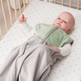 Bébé dans un berceau gris clair, gigoteuse verte, un bras en l’air.