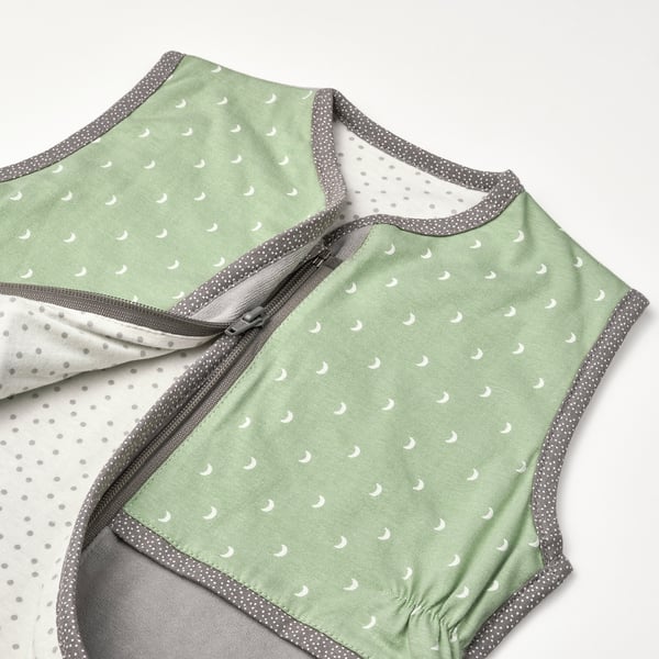 Gros plan d’un sac de couchage vert doux avec imprimé lune et bordure grise, mettant en valeur les détails de la fermeture éclair.