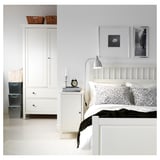 Chambre soignée avec armoire LERSTA blanche, lampe réglable, lit fait, art mural et paniers.