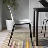 Chaise empilable blanche avec pieds noirs sur tapis rayé coloré près de la table à manger.