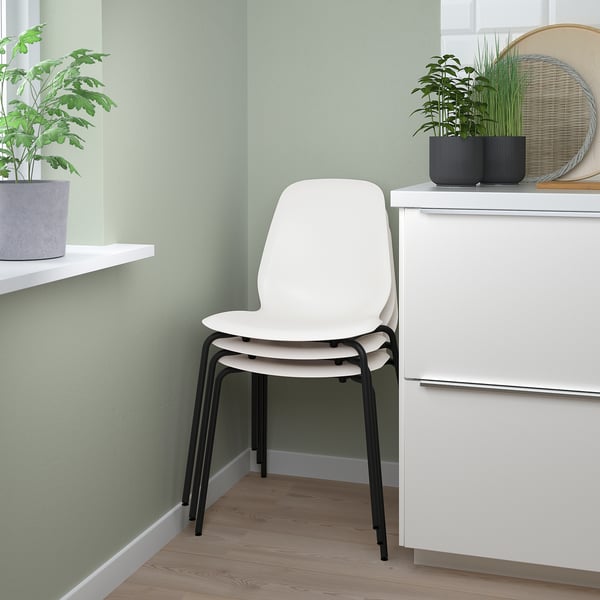 Pile de trois chaises LIDÅS blanches contre mur végétal, adaptées à une utilisation en intérieur.