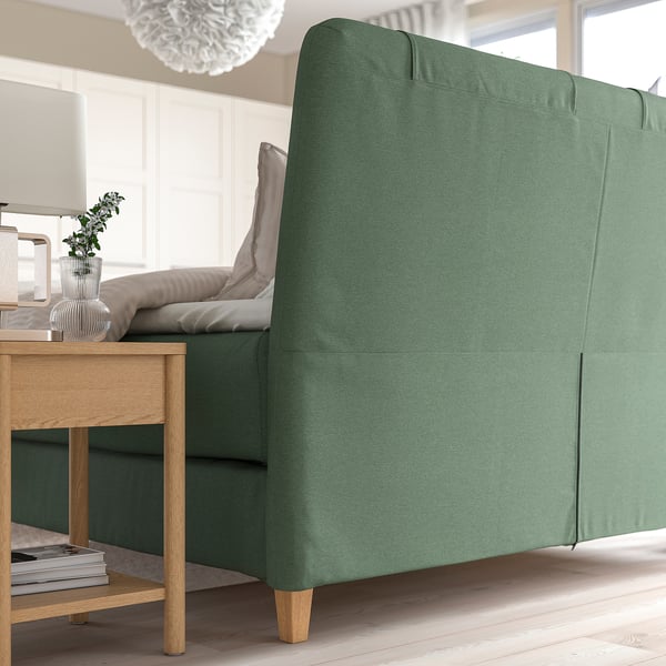Lit divan vert avec tête de lit inclinée, coussins pour plus de confort et pieds en bois dans une chambre à coucher confortable.