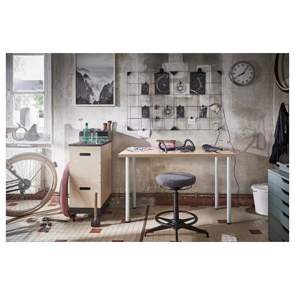 Atelier de style industriel avec table blanche, tabouret gris, horloge murale, vélo et outils.