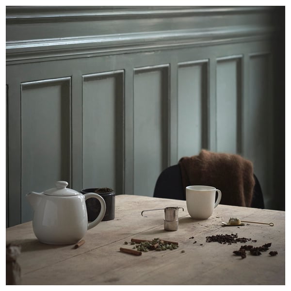 Installation de thé confortable sur une table en bois avec mur bleu. Bouilloire, passoire, tasse, thé et cannelle.
